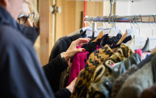 00015-Next-Vintage-Belgioioso-selezione-capi-vintage Visitatrice osserva capi d’abbigliamento vintage appesi su stand espositivo